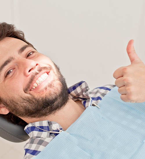 Man leaning back in dental chair giving thumbs up