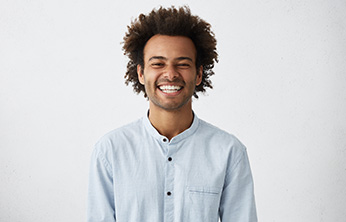 Man in button-up shirt standing in front of wall and smiling