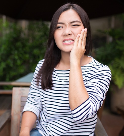 Woman in striped shirt rubbing jaw due to discomfort