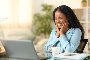 Woman sitting at laptop rubbing jaw in pain