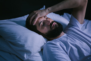 Man with sleep apnea lying in bed and holding hand on forehead